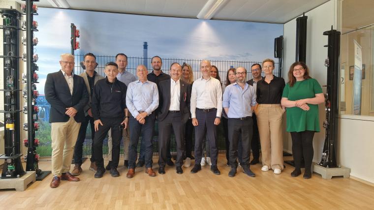 Gruppe von zwölf Personen in einem Raum mit Holzboden und Wandbild eines...