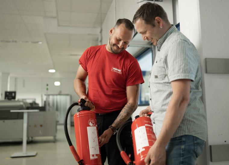 Zwei Männer, die jeweils auf einen Feuerlöscher schauen, die sie in der Hand...