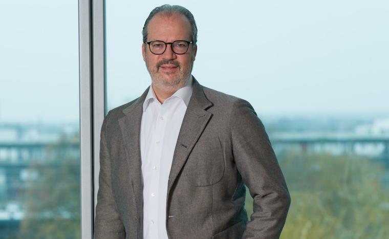 Mittelalter Mann mit grauem Sakko vor Fensterfront