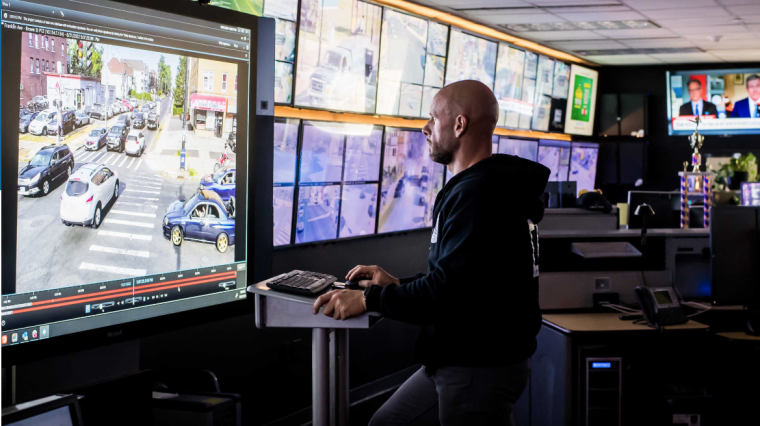 Mann mit Hoody an Stehpult vor Monitor in einer Leitstelle