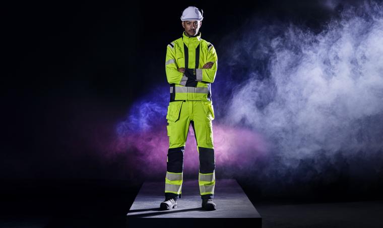 Person in kompletter Multinorm-Schutzkleidung steht auf einer Plattform vor...