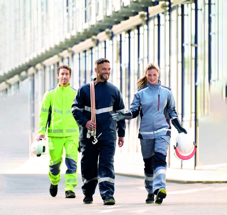 Drei Fachkräfte in Warn- und Schutzkleidung gehen auf einem Industriegelände...