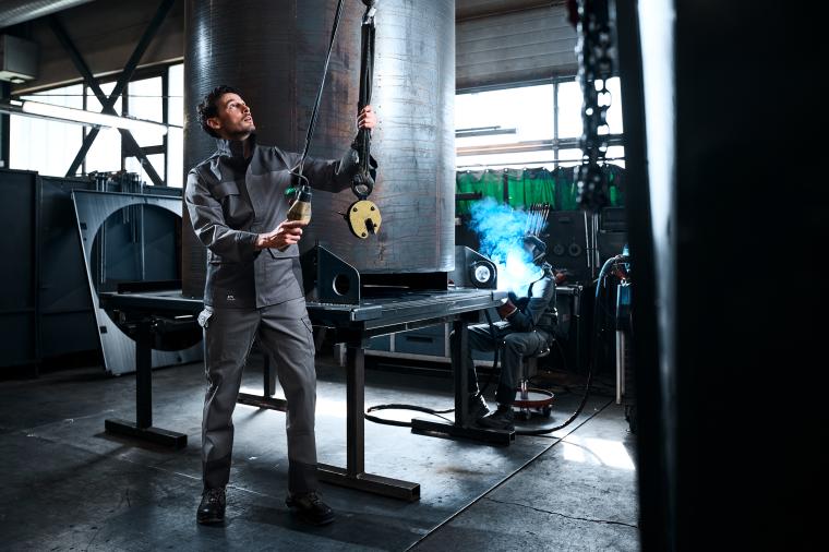 Eine Person in Arbeitskleidung bedient in einer industriellen Werkhalle einen...